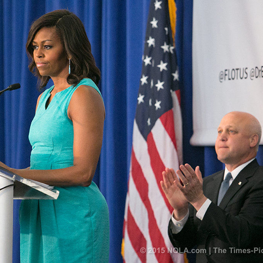 image of Michelle Obama behind a podium, addressing a crowd, with former Louisiana mayor Mitch Landrieu standing behind her and applauding
