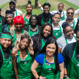 photo of a group of starbucks baristas, all dressed in their green aprons and smiling at the camera