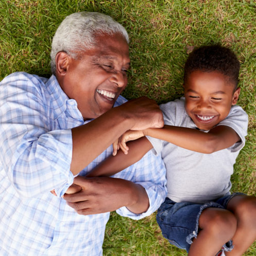 a kinship caregiver and a little boy lay on the grass together smiling